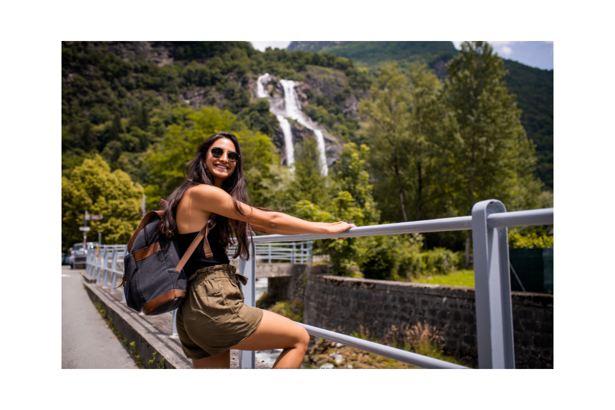 A solo traveler smiling while leaning on a railing near a waterfall in a natural setting.