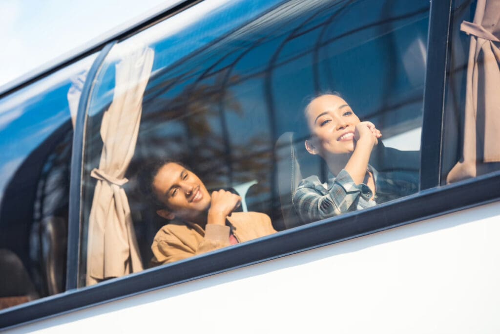 Low Budget Airlines, two individuals smiling while seated inside a bus, visible through the window.